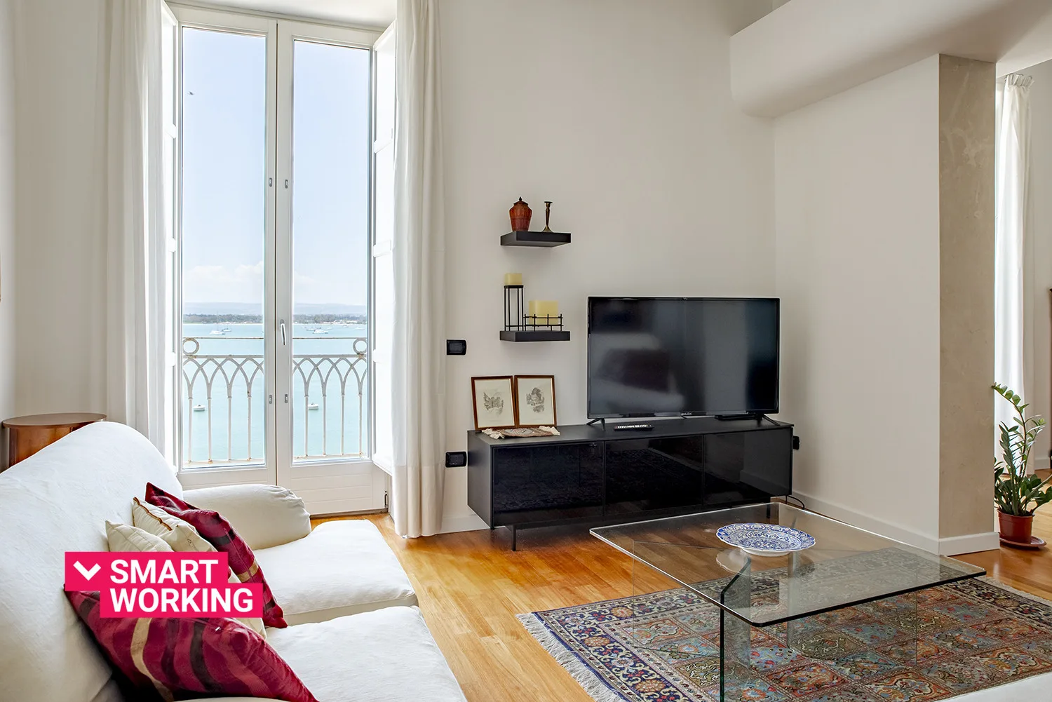 A living room with a television, seating, and tall windows overlooking the water.