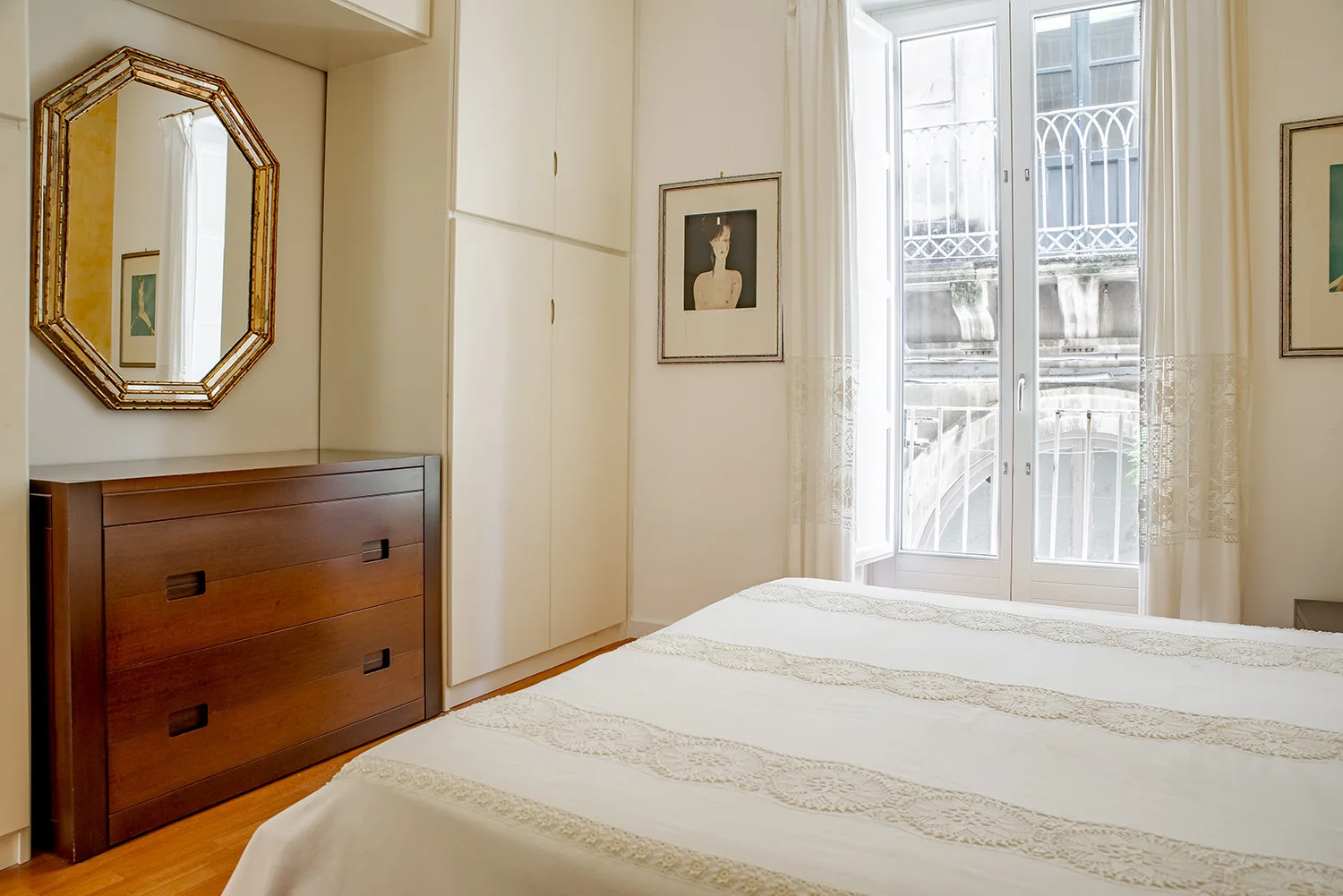 A bedroom with a neatly made bed, a dresser, and tall windows.