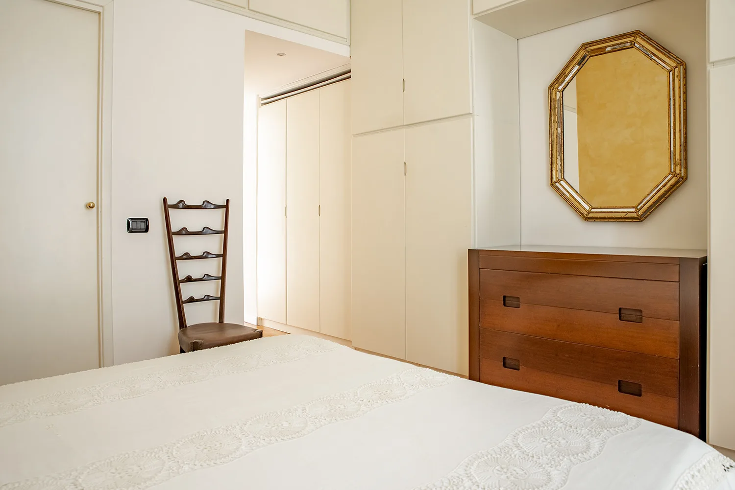 A bedroom with a bed, a wooden dresser, and a wall mirror.