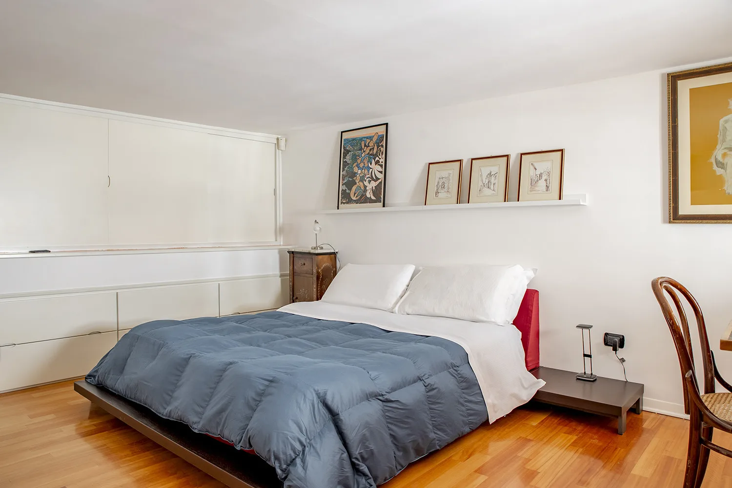 Bedroom with a bed covered in a blue-gray duvet and framed artwork on the wall.
