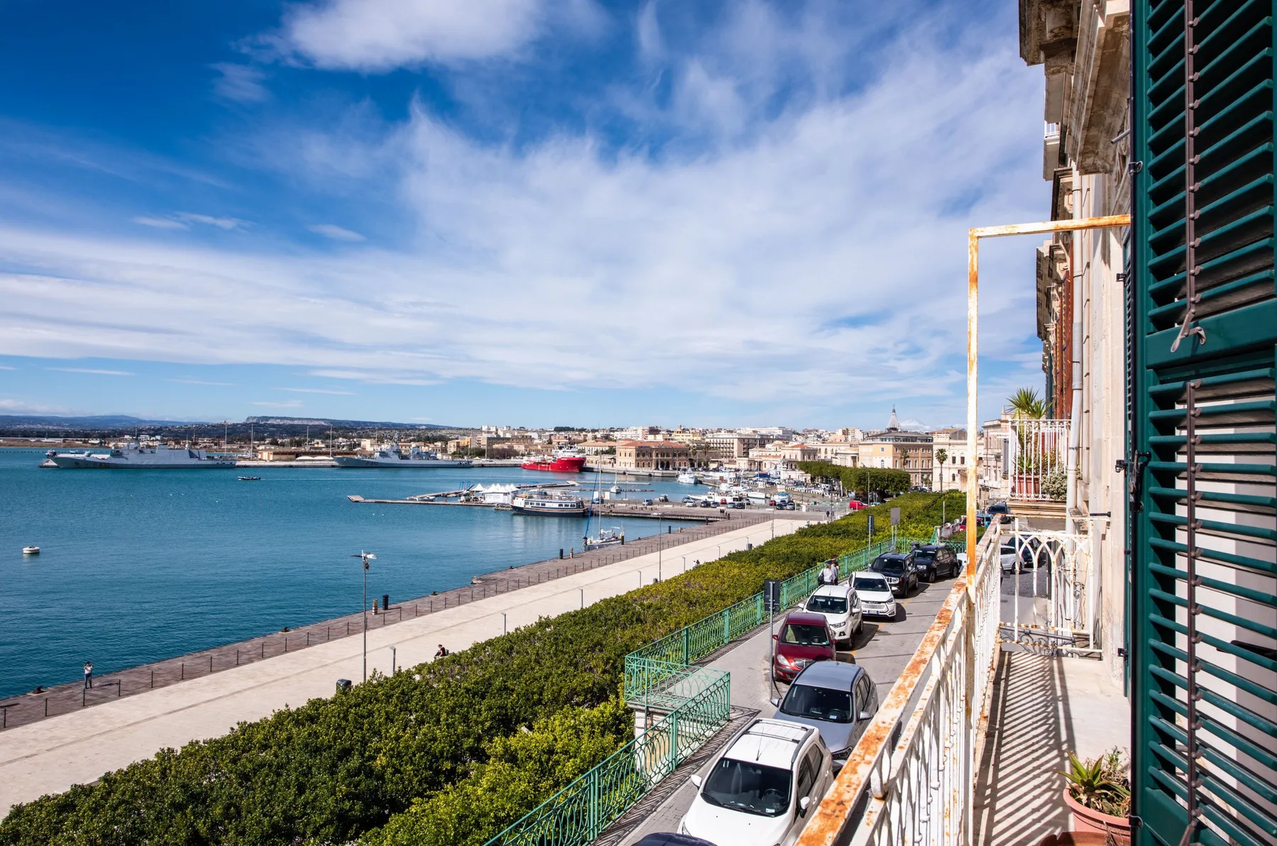 Coastal waterfront view from a balcony, with boats in the harbor and buildings along the shore.