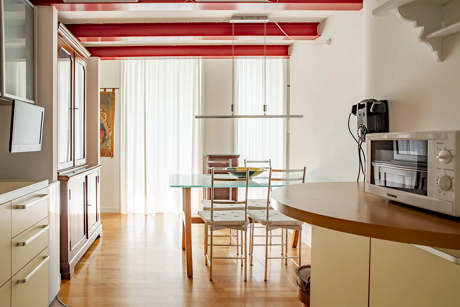 A bright dining area with a glass table and chairs beside a kitchenette.