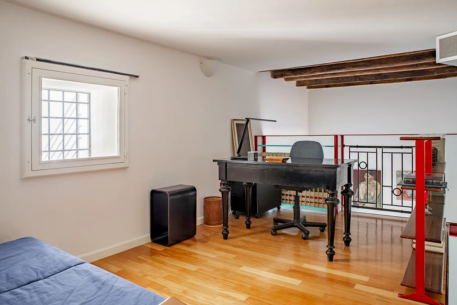 A bright room with a piano, desk chair, and blue bedding beside the window.