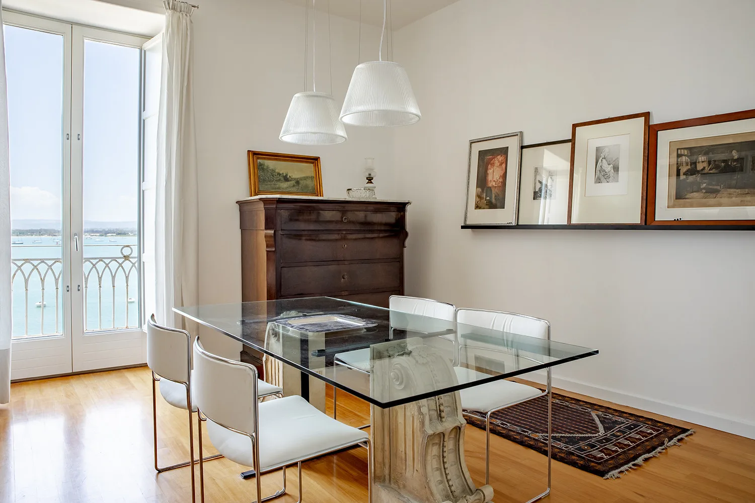 A bright dining room with a glass table, chairs, and framed artwork.