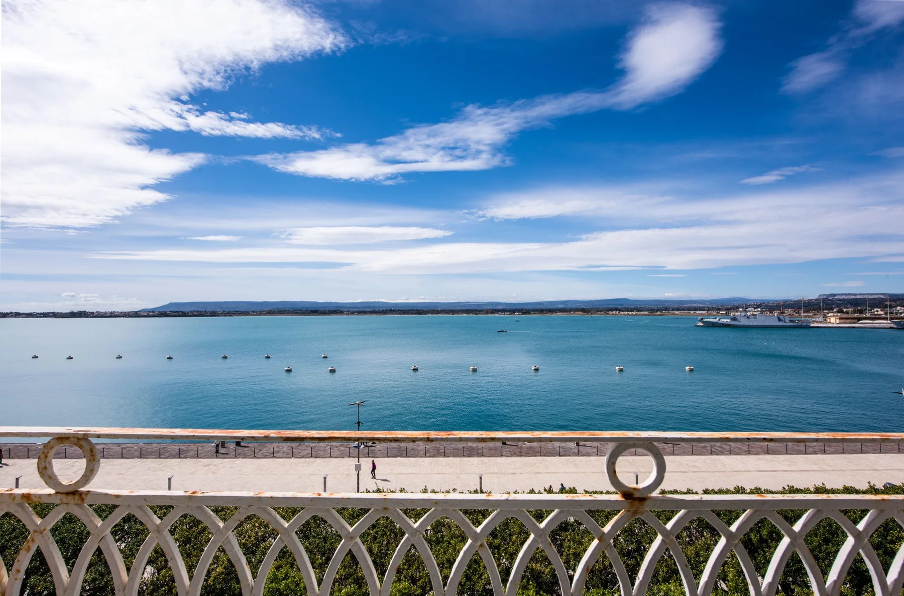 A view across a bay from a seaside promenade, with boats offshore.