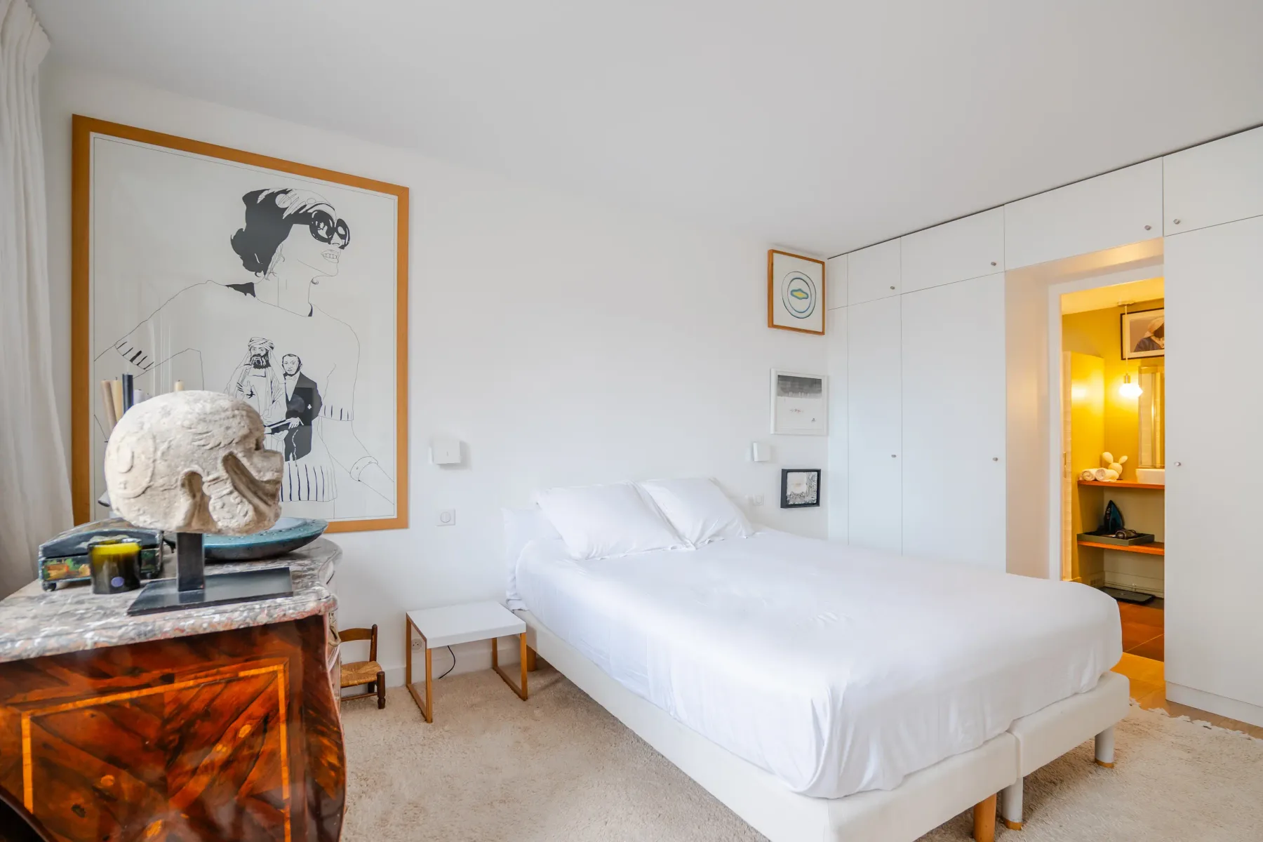 Un dormitorio luminoso con una cama blanca y una obra enmarcada.