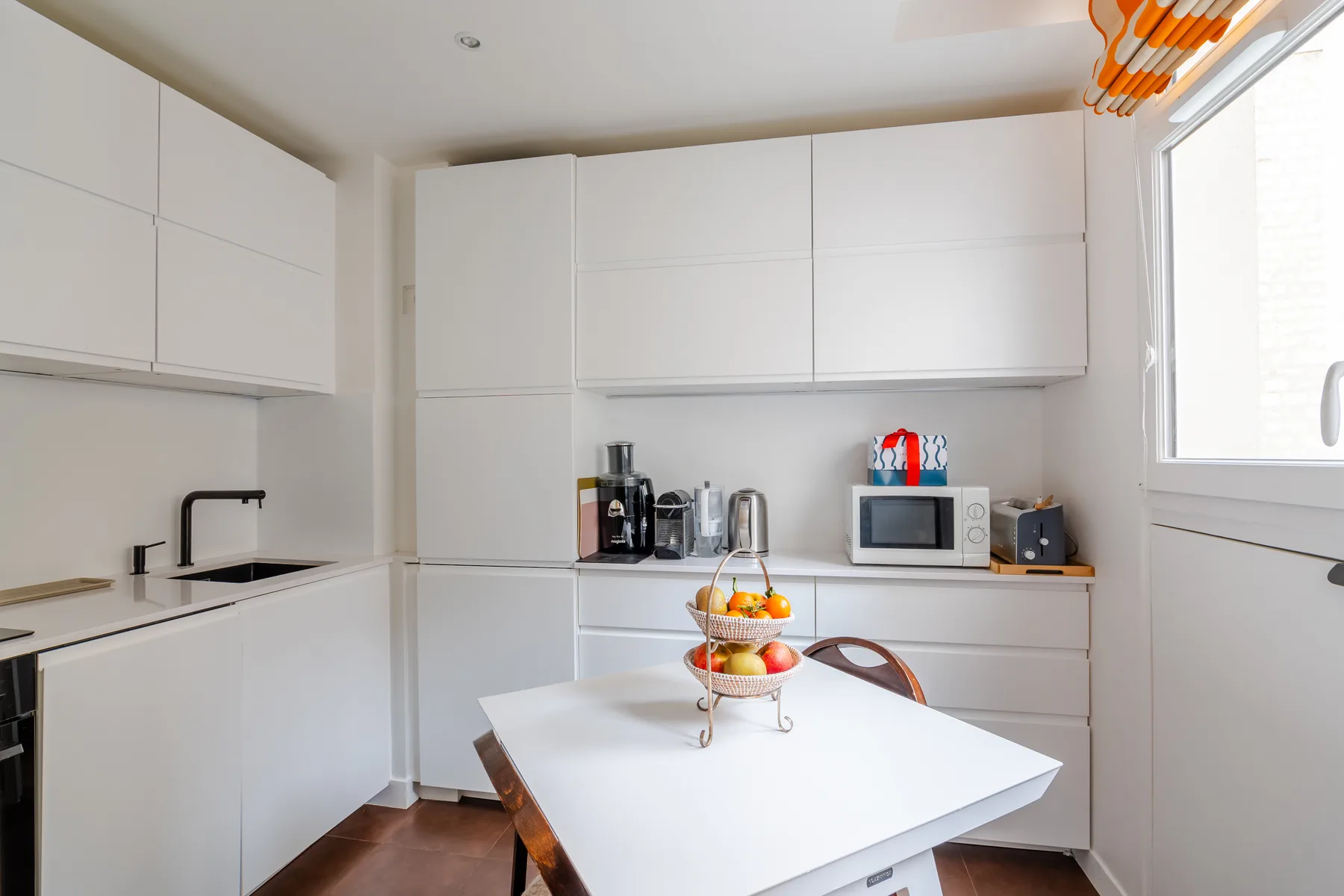 Una cocina luminosa con gabinetes blancos y una mesa de comedor con fruta.