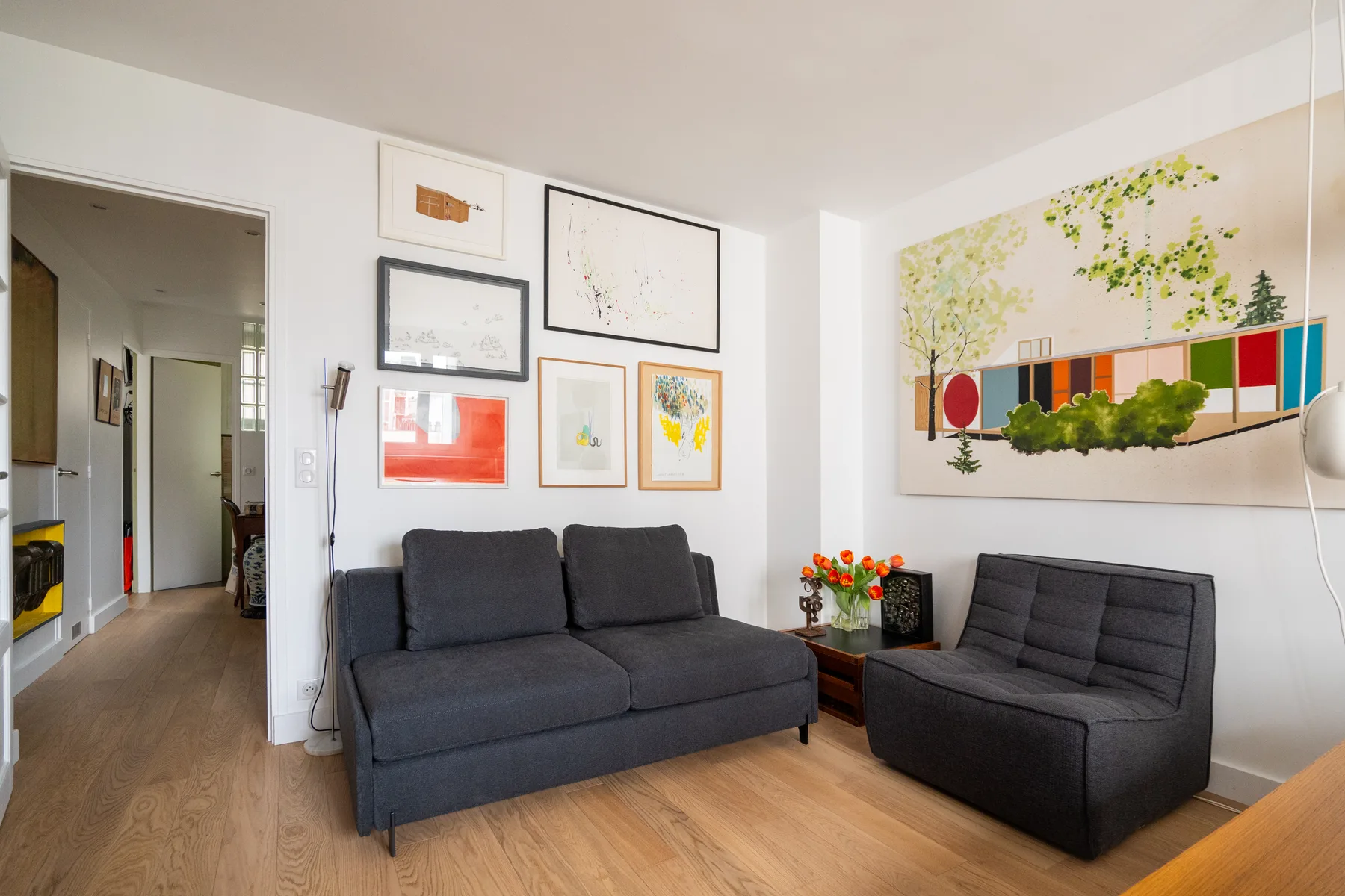 A bright living room with dark seating, framed artwork, and a colorful wall mural.