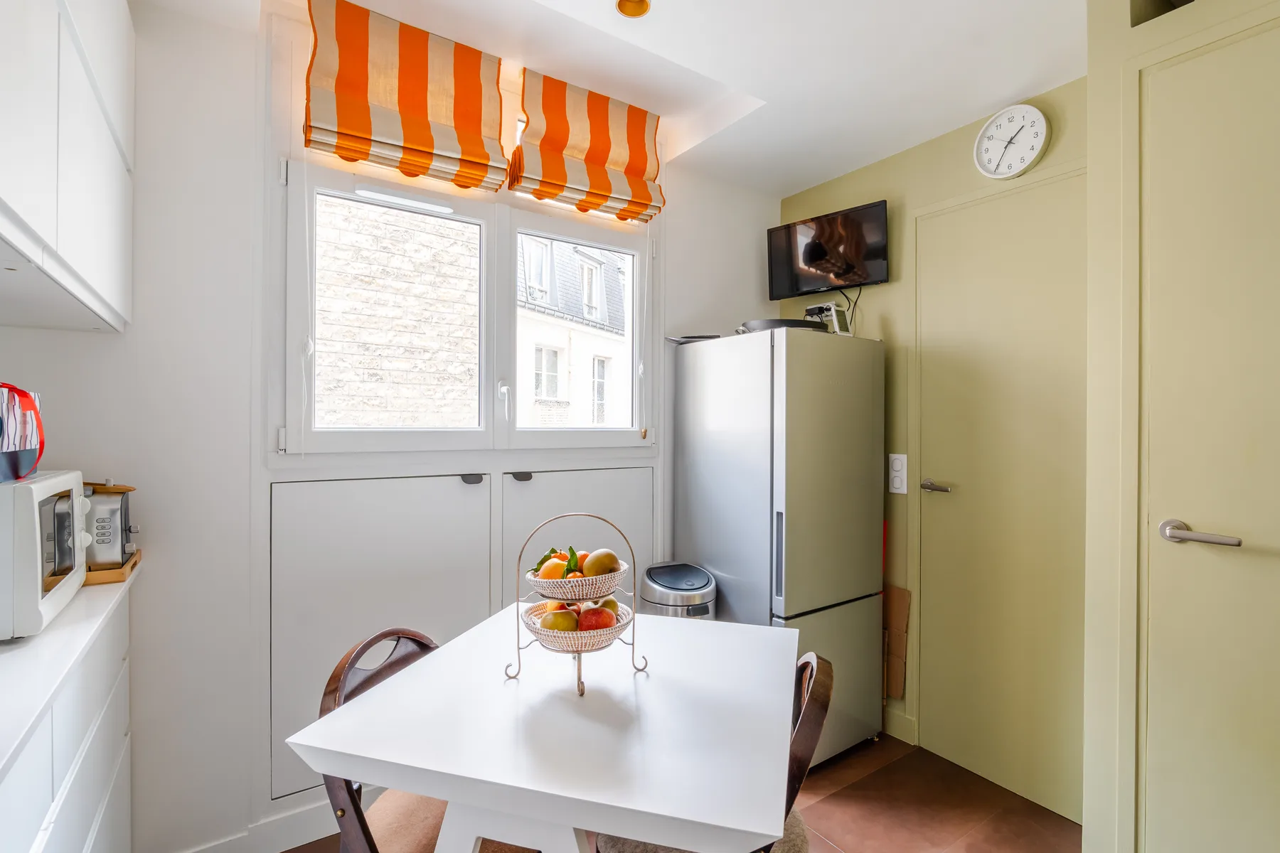 Una cocina luminosa con una mesa blanca y una cortina naranja a rayas.