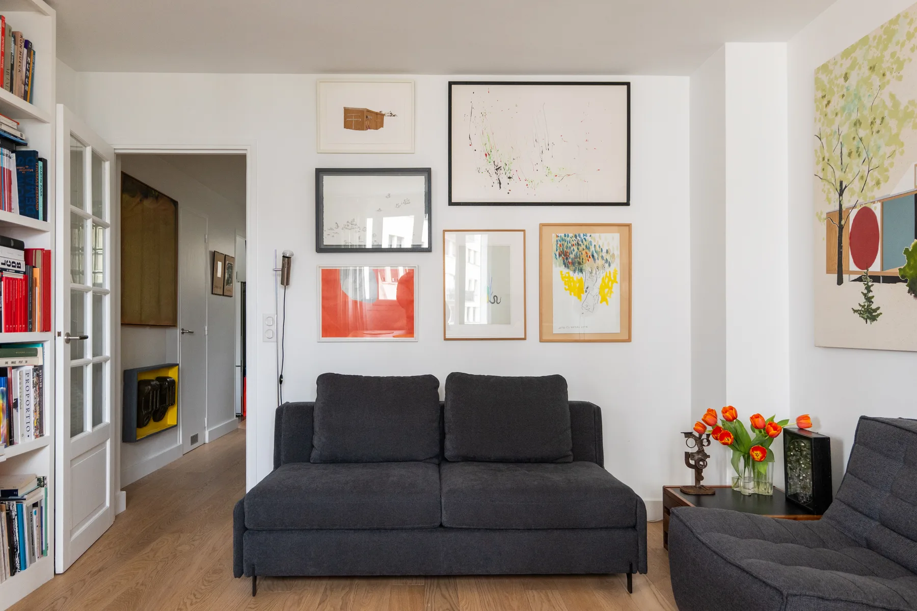 Una sala de estar con asientos oscuros, cuadros enmarcados y flores sobre una mesa auxiliar.