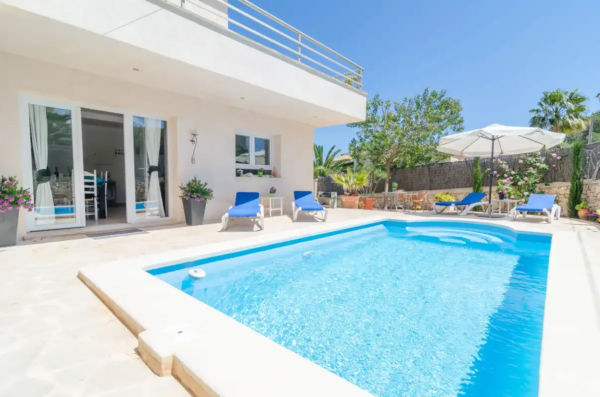 A swimming pool fills a sunny patio beside a white building and outdoor seating.