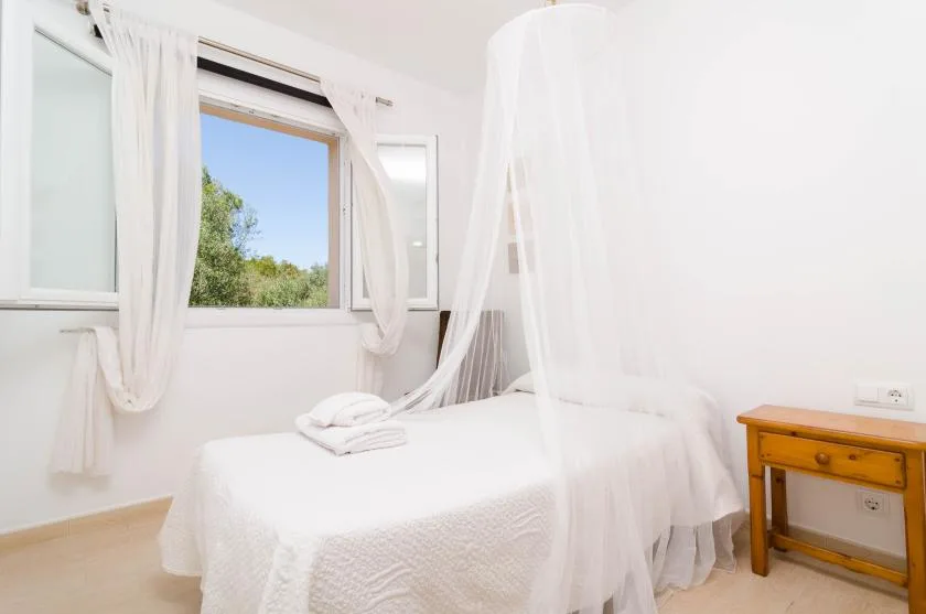 A bright bedroom with a white bed draped in sheer canopy curtains.