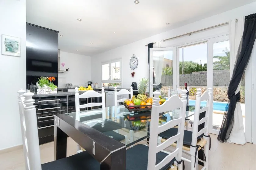 A bright dining area with a glass table and large windows overlooking a pool.