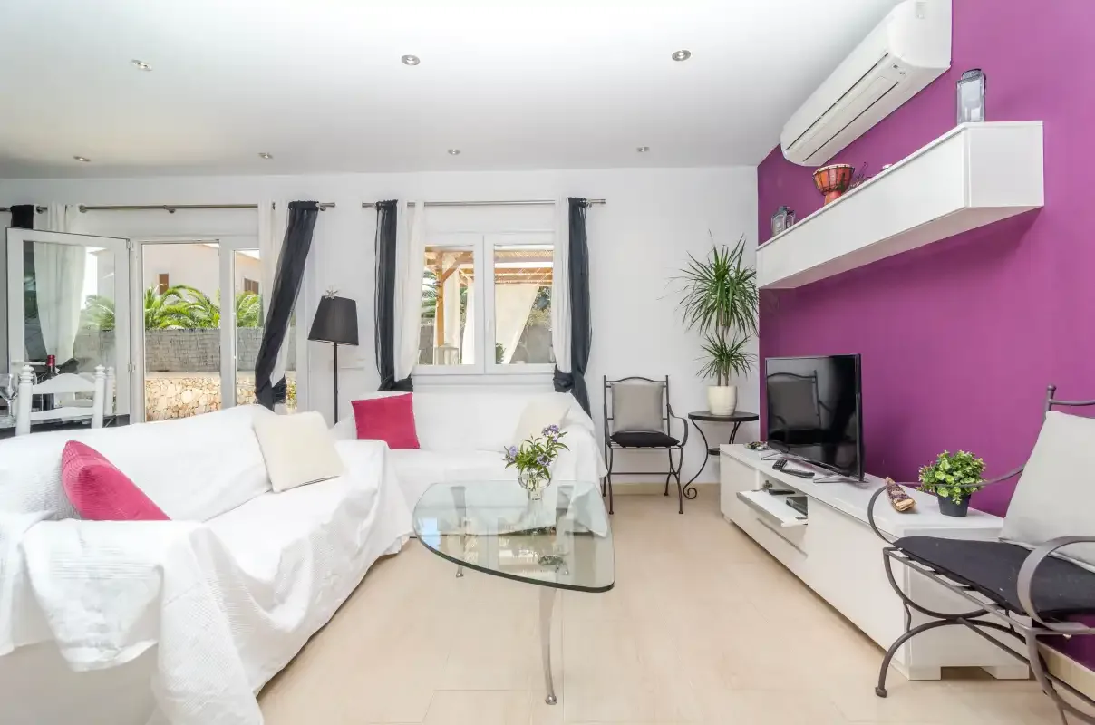 A bright living room with white seating, a glass coffee table, and a television.
