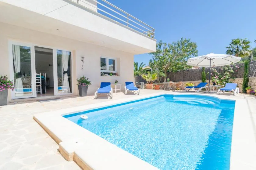 An outdoor swimming pool sits beside a modern house and patio seating.