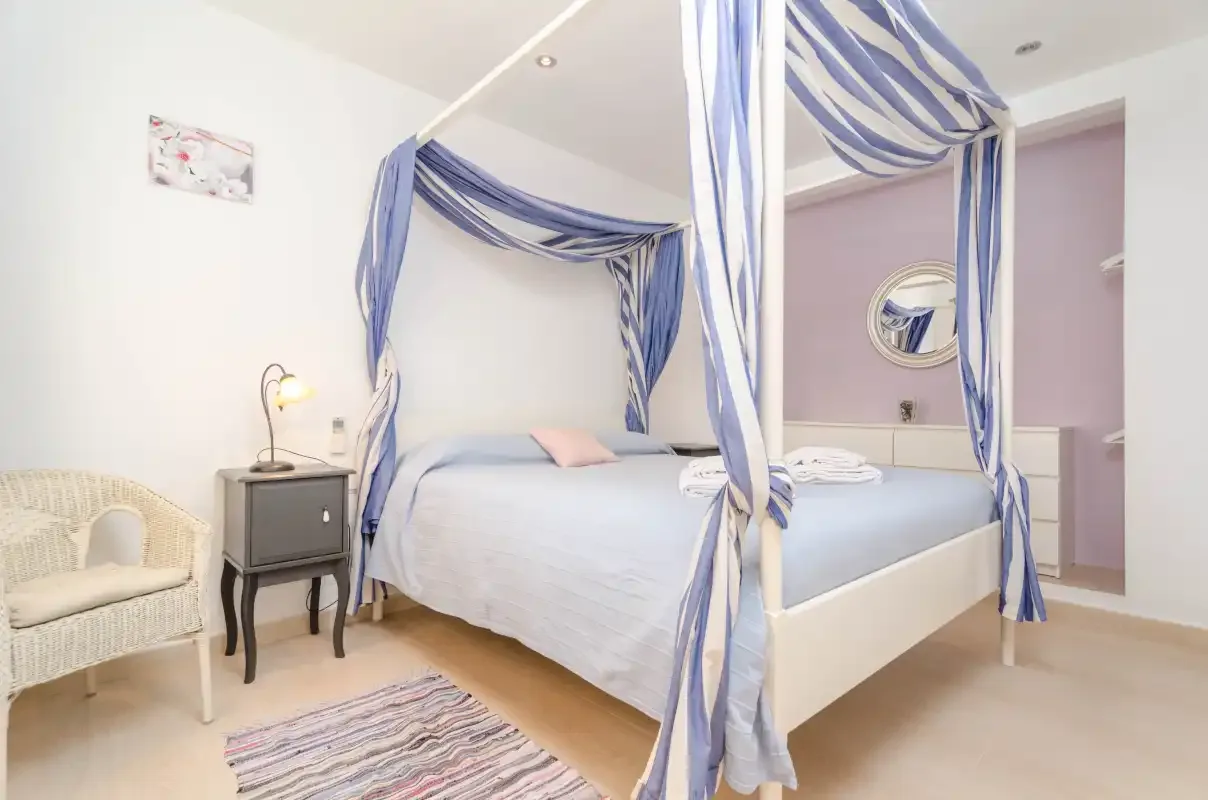 A bedroom with a canopy bed, a wicker chair, and a small bedside table.
