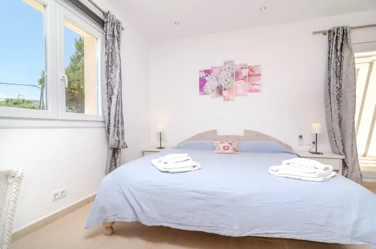 A bright bedroom with a neatly made bed and windows on two walls.