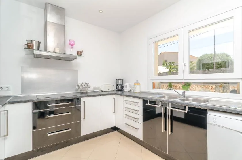 A bright modern kitchen with white cabinets, dark drawers, and a stainless steel range hood.