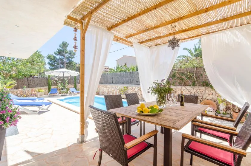 Una zona de comedor exterior a la sombra da a un patio con piscina.
