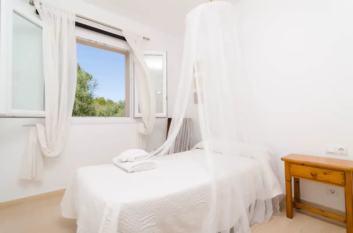 A bright bedroom with a white bed and sheer canopy curtains.
