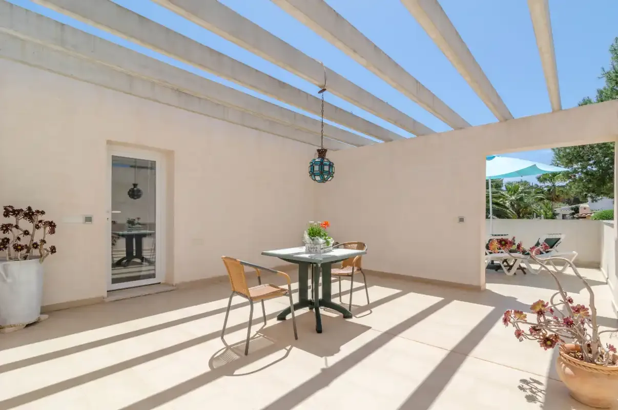 A shaded outdoor dining area with a table and chairs beneath a pergola.