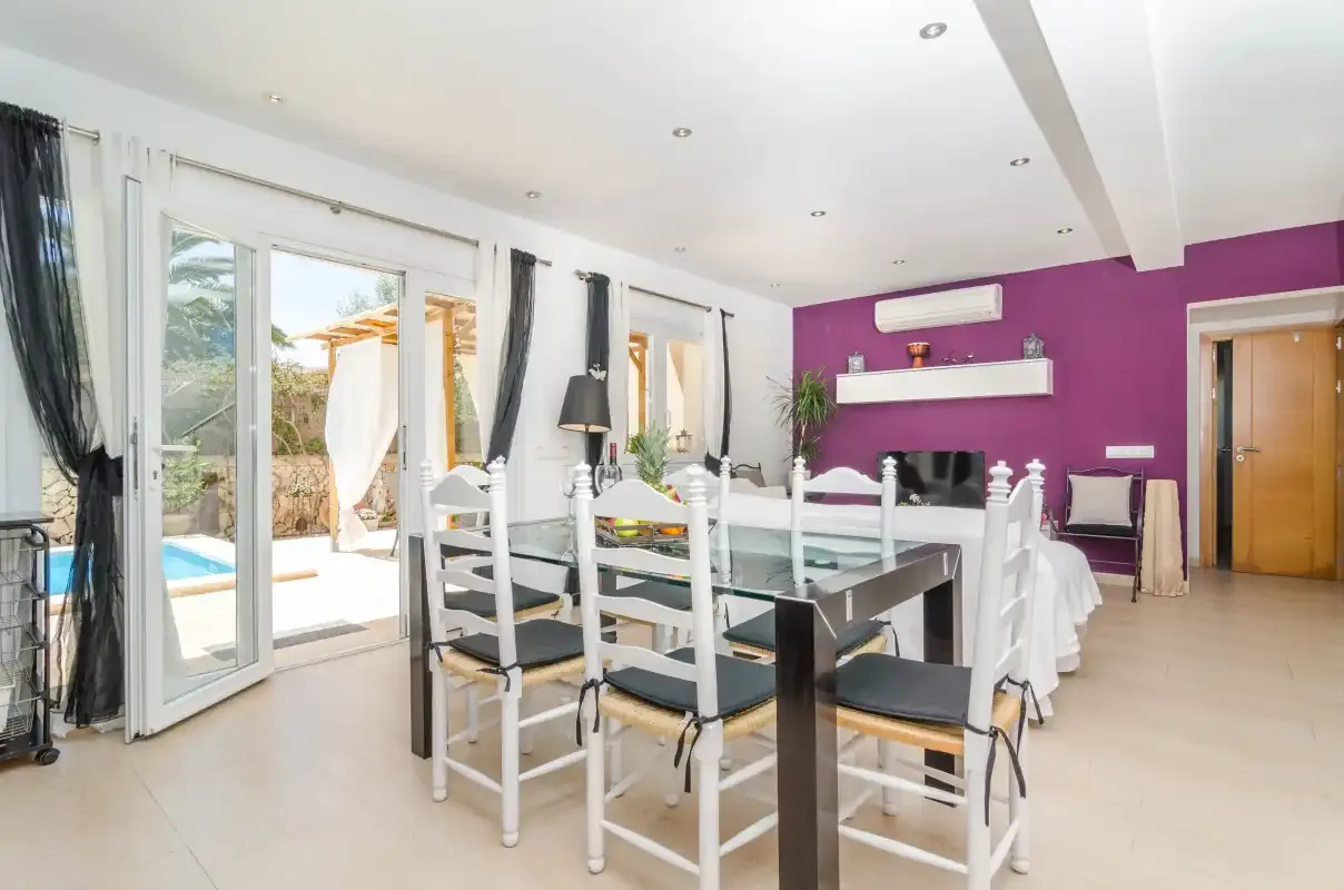 A bright dining area with a long table beside glass doors opening onto a patio.
