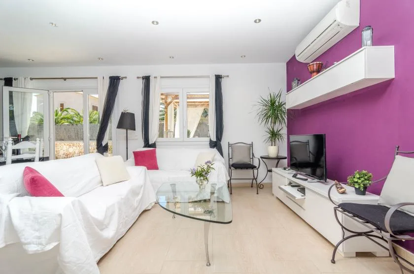 A bright living room with seating, a glass coffee table, and a television.