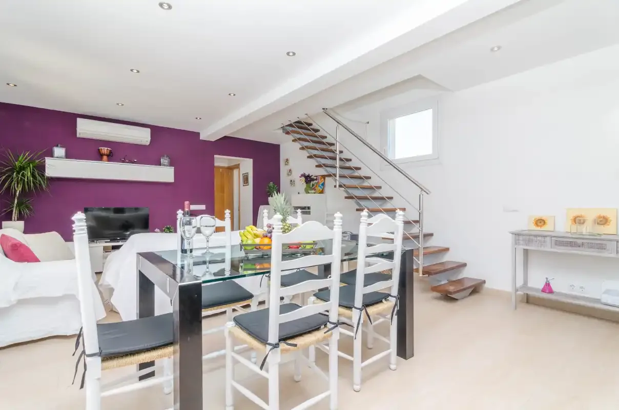 A dining and living area with a glass table and staircase.