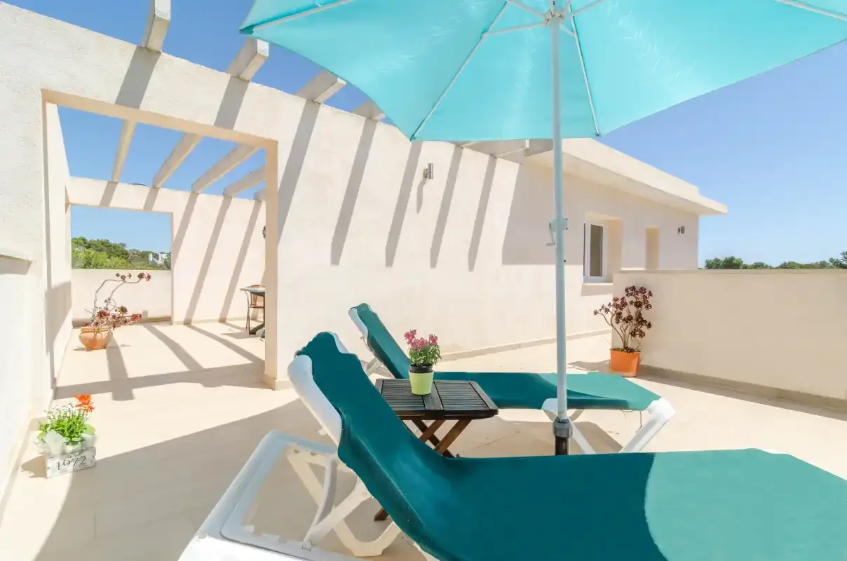 A sunny terrace with turquoise loungers and a large shade umbrella.