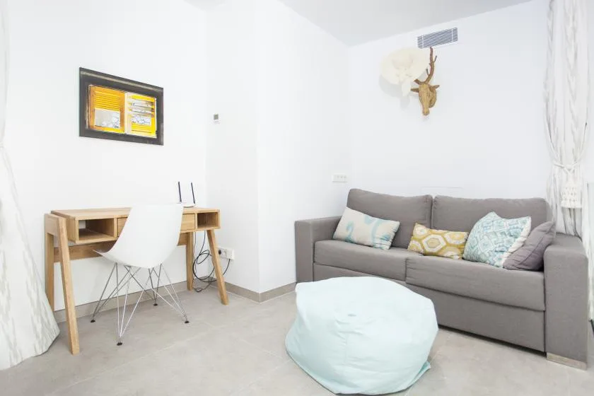 Una sala luminosa con un sofá gris y un escritorio pequeño.