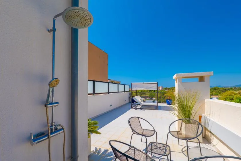 Una terraza en la azotea tiene asientos metálicos, una mesa y una ducha exterior.