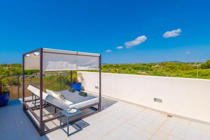 Una terraza en la azotea con una cama de día sombreada y vistas a colinas verdes.
