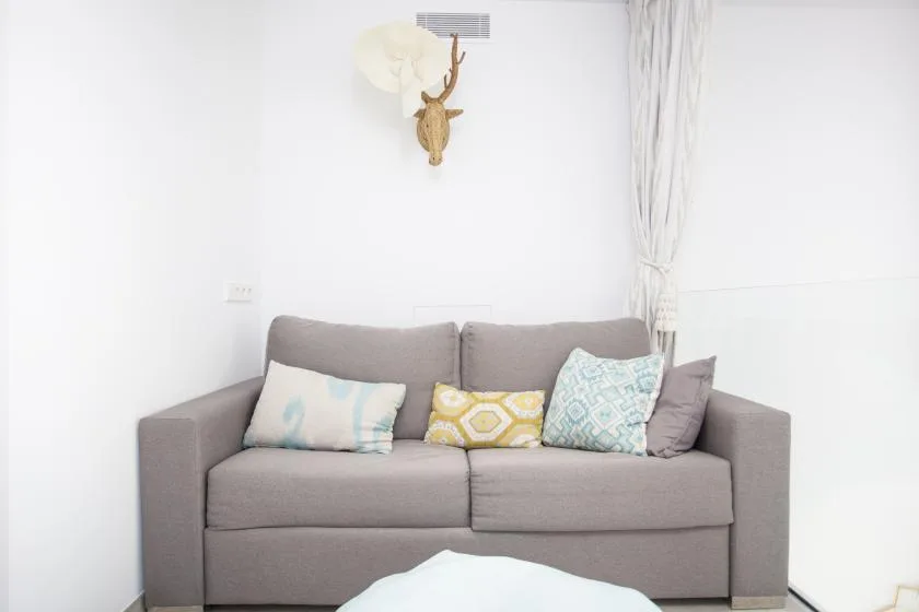 Un sofá gris con cojines de colores está junto a una pared blanca.