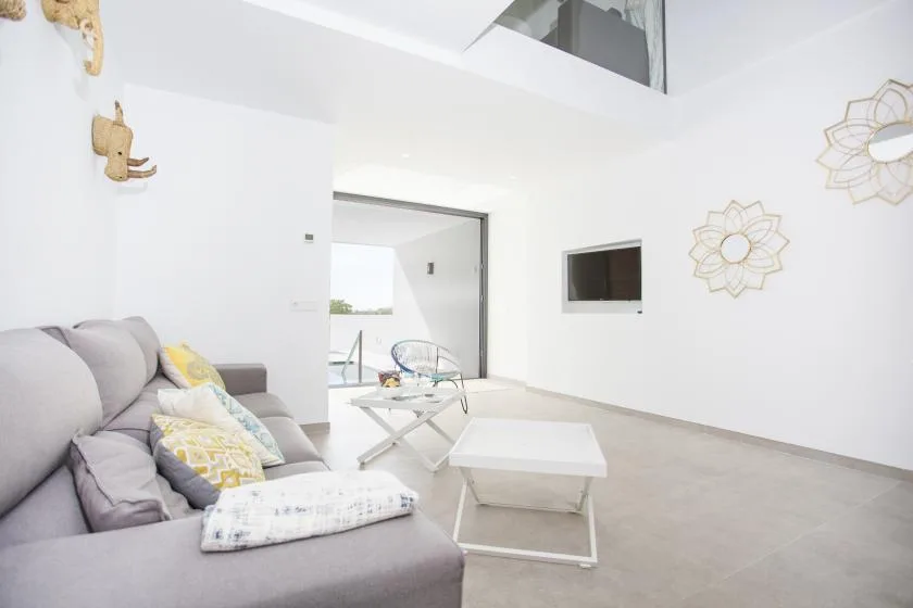 Una sala de estar luminosa con asientos, una mesa de centro y un televisor en la pared.