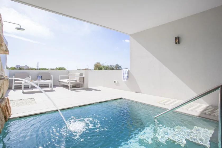 Una piscina al aire libre junto a un patio soleado con asientos.