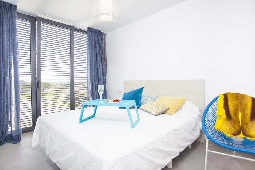 Un dormitorio con una cama blanca, cojines de colores y una silla azul.