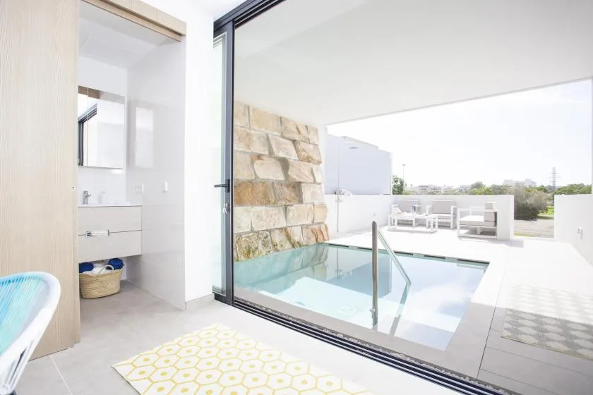 Una luminosa zona de piscina interior y exterior con puertas corredizas de vidrio y una pared de piedra.