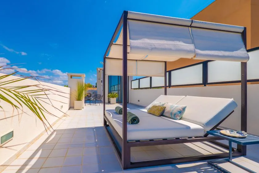 Una terraza soleada en la azotea con una cama de día a la sombra y cielo azul despejado.