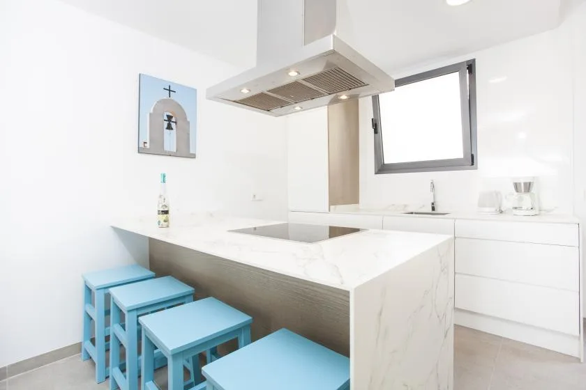 Una cocina moderna y luminosa con una isla blanca y taburetes azules.