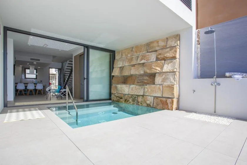 Una pequeña piscina interior está junto a una pared de piedra, con una ducha cerca.