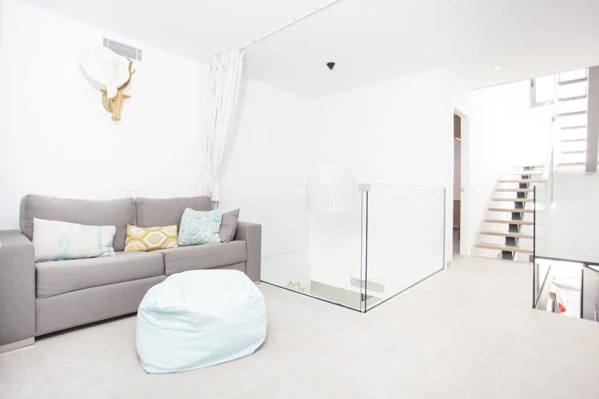 Una sala luminosa con asientos grises y una mampara de vidrio junto a una escalera.