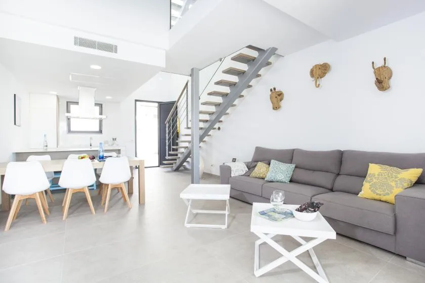Una luminosa sala de estar y comedor de concepto abierto, con asientos grises y una escalera.