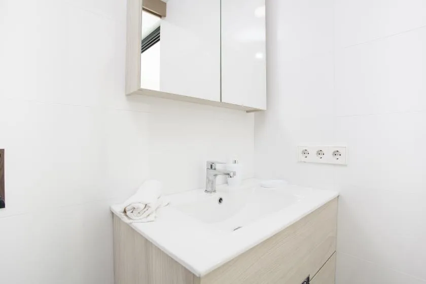 Un tocador de baño luminoso con lavabo, grifo y armario con espejo.