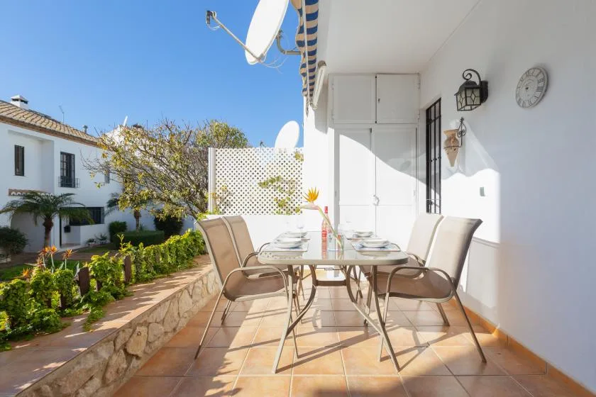 A sunny outdoor dining area with a table and chairs beside a garden.