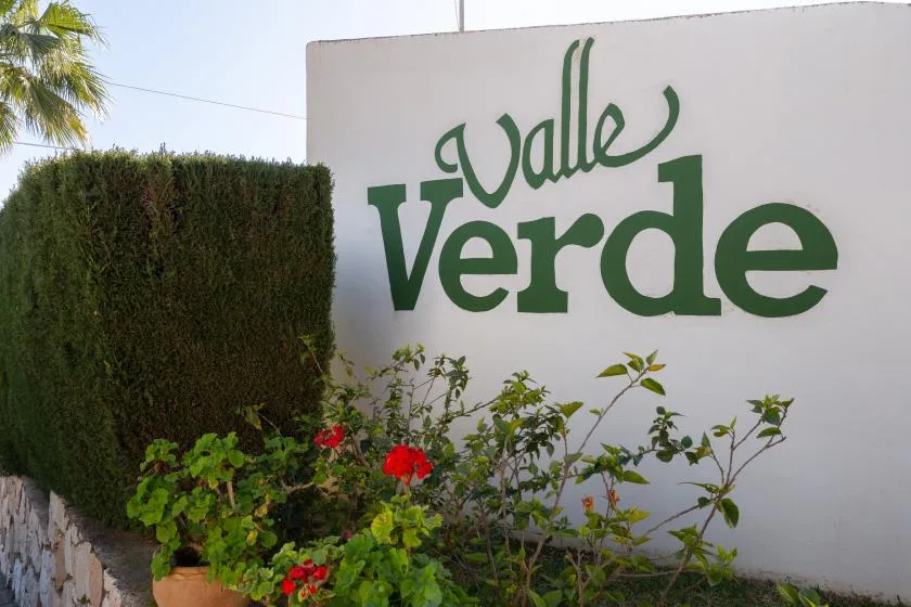 A white wall displays a green “Valle Verde” sign beside flowering plants.