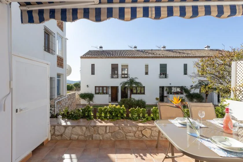 A sunny patio with outdoor seating overlooks a landscaped courtyard and white building.