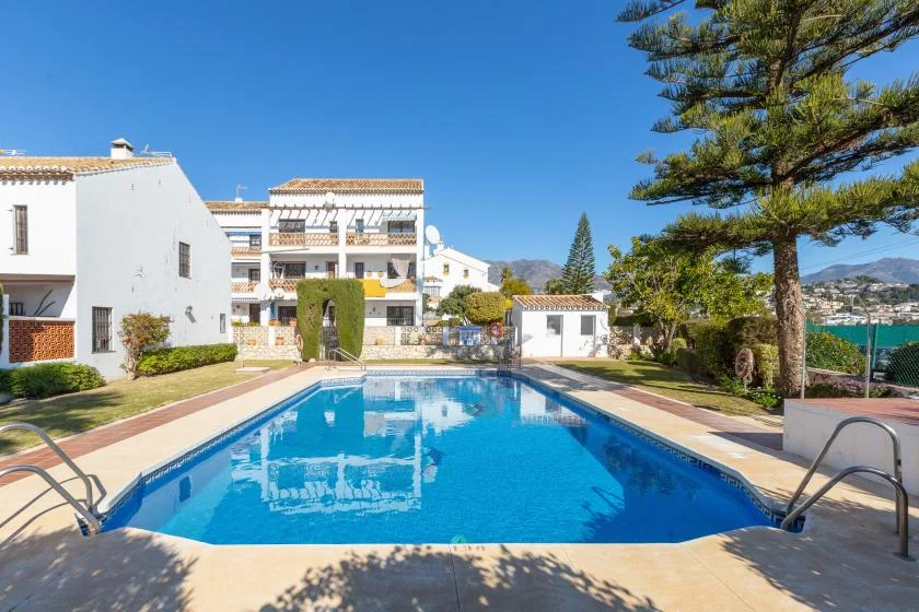An outdoor swimming pool sits in front of white apartment buildings and landscaped grounds.