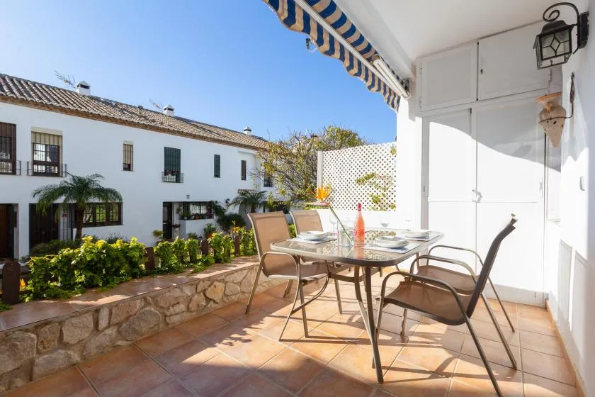 A tiled outdoor patio with a glass table and seating overlooks a white building.