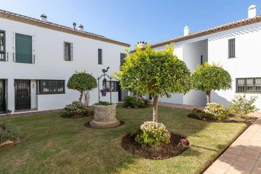 A landscaped courtyard with white buildings, trimmed trees, and a stone fountain.