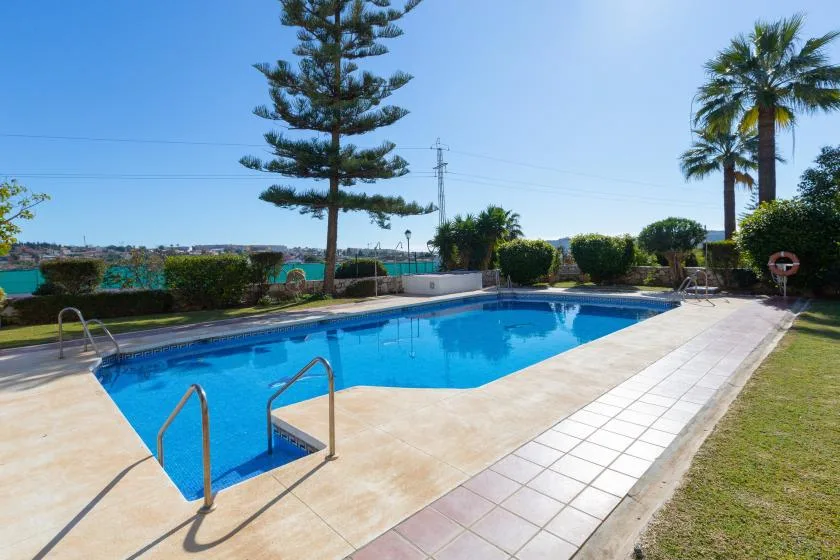 An outdoor swimming pool is surrounded by a tiled deck and greenery.